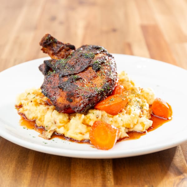 Grilled chicken thigh with mashed potatoes, carrots, and a rich sauce on a white plate.
