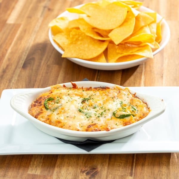 Baked queso dip with jalapeños and parsley, served with a bowl of tortilla chips.