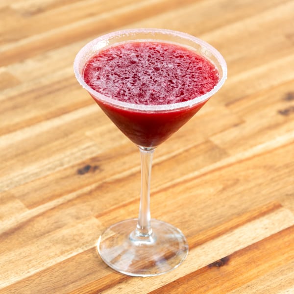 A vibrant red martini with a sugared rim sits on a warm wooden table.