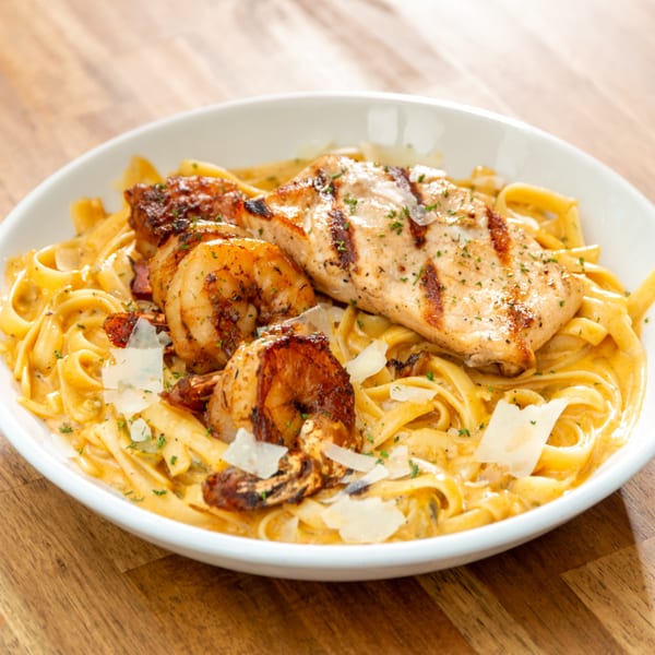 Creamy fettuccine pasta with grilled chicken, blackened shrimp, and parmesan cheese in a white bowl.