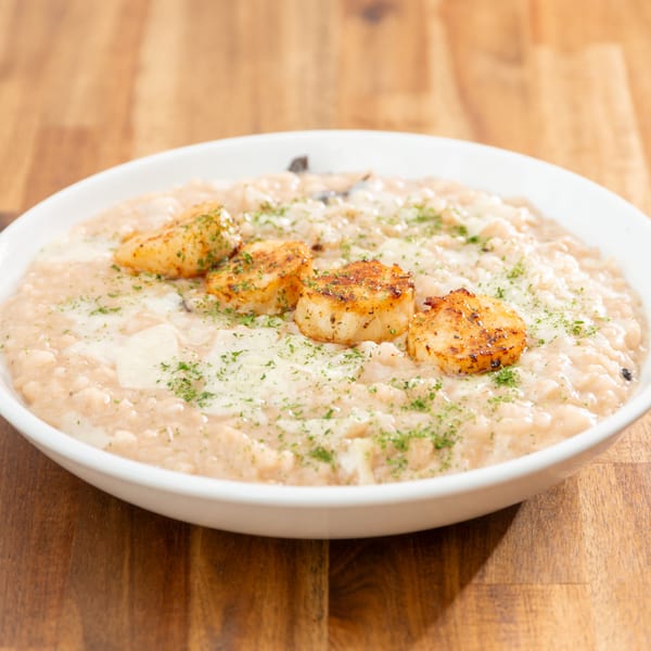 Creamy risotto topped with four pan-seared scallops, garnished with fresh parsley, on a wooden table.