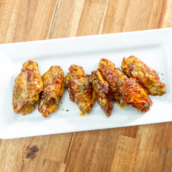 Seven glazed chicken wings, some with herbs, on a white rectangular plate on a wooden table.